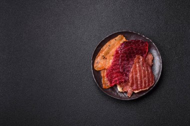 Kurutulmuş et, tuzlu, baharatlı ve otlu dilimler halinde koyu beton bir arka planda.