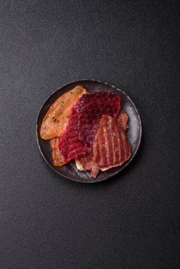 Kurutulmuş et, tuzlu, baharatlı ve otlu dilimler halinde koyu beton bir arka planda.