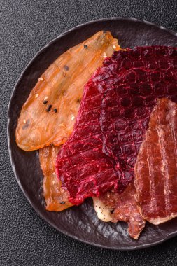 Kurutulmuş et, tuzlu, baharatlı ve otlu dilimler halinde koyu beton bir arka planda.