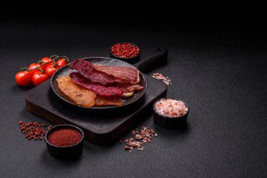 Kurutulmuş et, tuzlu, baharatlı ve otlu dilimler halinde koyu beton bir arka planda.