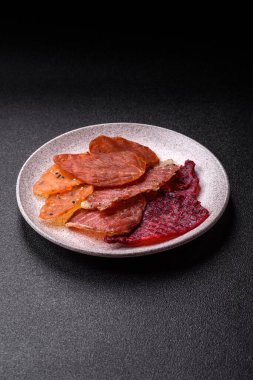 Kurutulmuş et, tuzlu, baharatlı ve otlu dilimler halinde koyu beton bir arka planda.