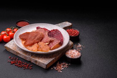 Kurutulmuş et, tuzlu, baharatlı ve otlu dilimler halinde koyu beton bir arka planda.