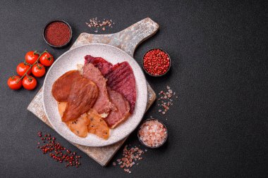 Kurutulmuş et, tuzlu, baharatlı ve otlu dilimler halinde koyu beton bir arka planda.