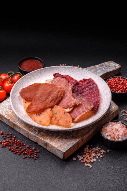 Kurutulmuş et, tuzlu, baharatlı ve otlu dilimler halinde koyu beton bir arka planda.