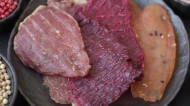 Kurutulmuş et, tuzlu, baharatlı ve otlu dilimler halinde koyu beton bir arka planda.