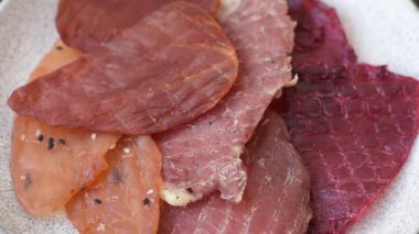 Kurutulmuş et, tuzlu, baharatlı ve otlu dilimler halinde koyu beton bir arka planda.