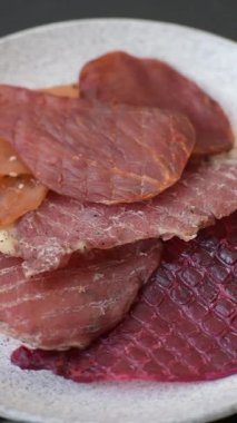 Kurutulmuş et, tuzlu, baharatlı ve otlu dilimler halinde koyu beton bir arka planda.