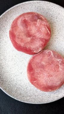 Two fresh slices of raw tuna fillet with spices and herbs on a dark concrete background