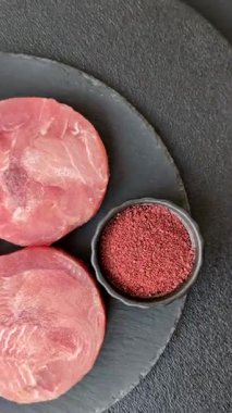 Two fresh slices of raw tuna fillet with spices and herbs on a dark concrete background