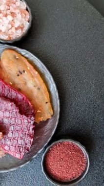 Kurutulmuş et, tuzlu, baharatlı ve otlu dilimler halinde koyu beton bir arka planda.