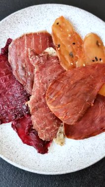 Kurutulmuş et, tuzlu, baharatlı ve otlu dilimler halinde koyu beton bir arka planda.