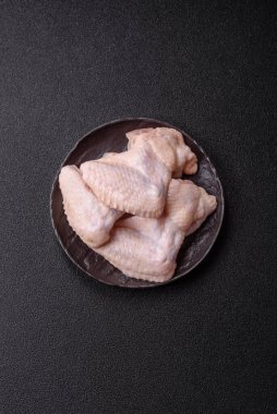 Raw chicken wings with salt, spices and herbs on a wooden cutting board on a dark concrete background