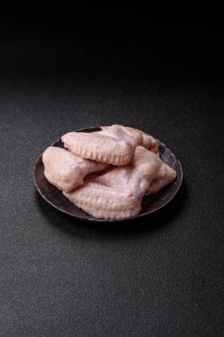 Raw chicken wings with salt, spices and herbs on a wooden cutting board on a dark concrete background