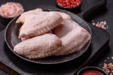 Raw chicken wings with salt, spices and herbs on a wooden cutting board on a dark concrete background