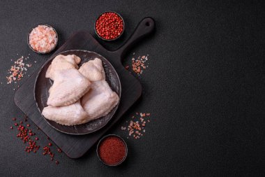Raw chicken wings with salt, spices and herbs on a wooden cutting board on a dark concrete background