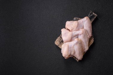 Raw chicken wings with salt, spices and herbs on a wooden cutting board on a dark concrete background