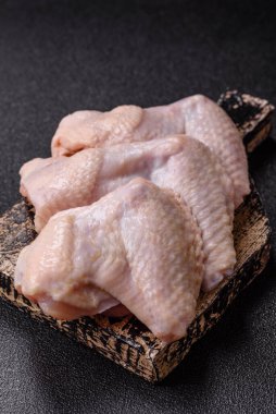 Raw chicken wings with salt, spices and herbs on a wooden cutting board on a dark concrete background