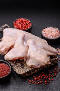 Raw chicken wings with salt, spices and herbs on a wooden cutting board on a dark concrete background