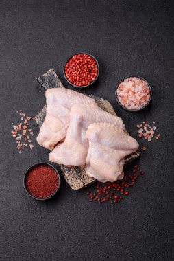 Raw chicken wings with salt, spices and herbs on a wooden cutting board on a dark concrete background