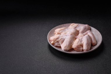 Raw chicken wings with salt, spices and herbs on a wooden cutting board on a dark concrete background