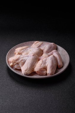 Raw chicken wings with salt, spices and herbs on a wooden cutting board on a dark concrete background