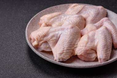 Raw chicken wings with salt, spices and herbs on a wooden cutting board on a dark concrete background