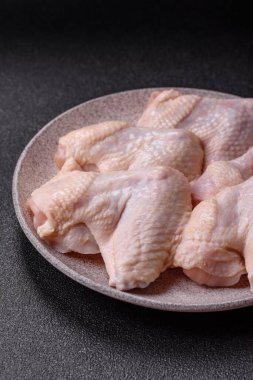 Raw chicken wings with salt, spices and herbs on a wooden cutting board on a dark concrete background