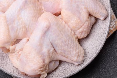 Raw chicken wings with salt, spices and herbs on a wooden cutting board on a dark concrete background