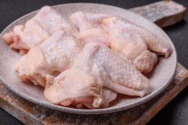 Raw chicken wings with salt, spices and herbs on a wooden cutting board on a dark concrete background