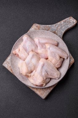 Raw chicken wings with salt, spices and herbs on a wooden cutting board on a dark concrete background