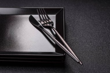 Empty ceramic round plate on dark textured concrete background. Cutlery, preparation for dinner