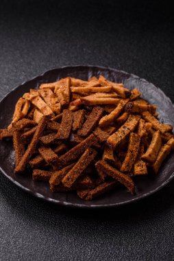 Koyu beton arka planda tohum ve tahıllı, tuzlu, baharatlı ve otlu ev yapımı kahverengi ekmek krakerleri veya kızarmış ekmekler.