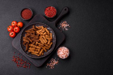 Koyu beton arka planda tohum ve tahıllı, tuzlu, baharatlı ve otlu ev yapımı kahverengi ekmek krakerleri veya kızarmış ekmekler.