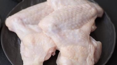 Raw chicken wings with salt, spices and herbs on a wooden cutting board on a dark concrete background