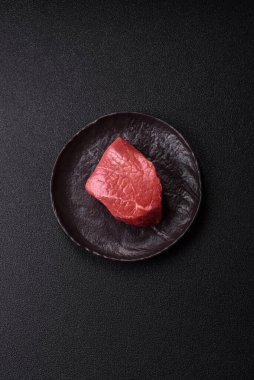 Koyu beton zeminde tuzlu ve baharatlı çiğ sığır filetosu bifteği.