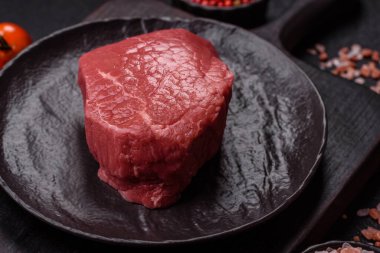 Koyu beton zeminde tuzlu ve baharatlı çiğ sığır filetosu bifteği.