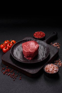 Koyu beton zeminde tuzlu ve baharatlı çiğ sığır filetosu bifteği.