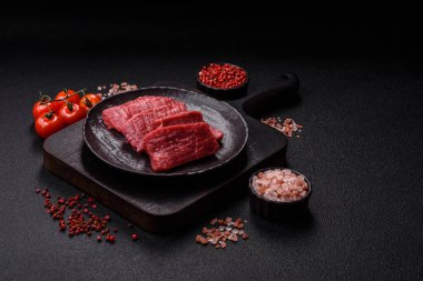 Çiğ sığır filetosu, koyu beton arka planda tuz ve baharatla dilimlenmiş.