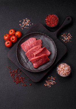Çiğ sığır filetosu, koyu beton arka planda tuz ve baharatla dilimlenmiş.