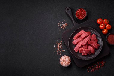 Çiğ sığır filetosu, koyu beton arka planda tuz ve baharatla dilimlenmiş.