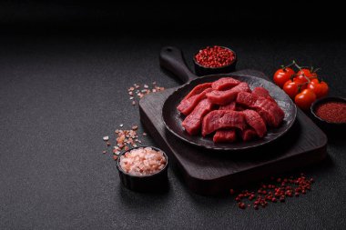 Çiğ sığır filetosu, koyu beton arka planda tuz ve baharatla dilimlenmiş.