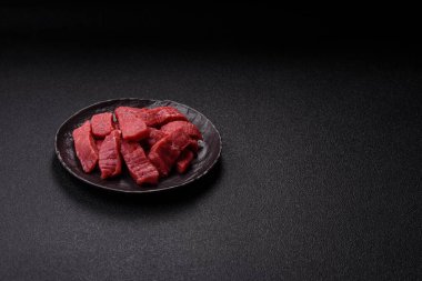 Çiğ sığır filetosu, koyu beton arka planda tuz ve baharatla dilimlenmiş.