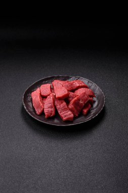 Çiğ sığır filetosu, koyu beton arka planda tuz ve baharatla dilimlenmiş.