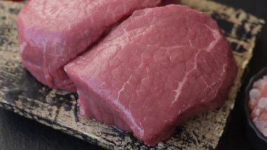 Koyu beton zeminde tuzlu ve baharatlı çiğ sığır filetosu bifteği.