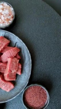 Çiğ sığır filetosu, koyu beton arka planda tuz ve baharatla dilimlenmiş.