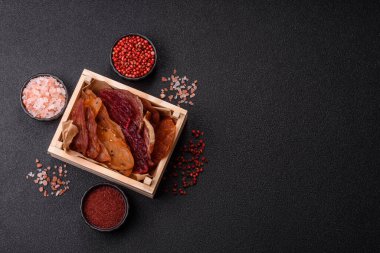 Kurutulmuş et, tuzlu, baharatlı ve otlu dilimler halinde koyu beton bir arka planda.