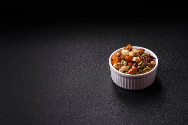 Ballı fındık, ceviz, fındık, çam fıstığı ve kurutulmuş meyveler koyu beton arka planda seramik kasede.