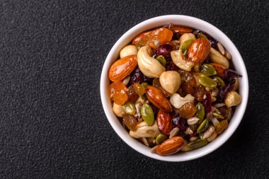 Ballı fındık, ceviz, fındık, çam fıstığı ve kurutulmuş meyveler koyu beton arka planda seramik kasede.