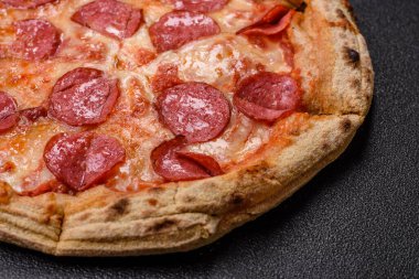 Pepperoni pizza with sausage, cheese, tomatoes, salt and spices on dark concrete background