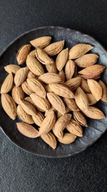 Kavrulmuş ya da çiğ badem fıstığı kabukta koyu beton arka planda.